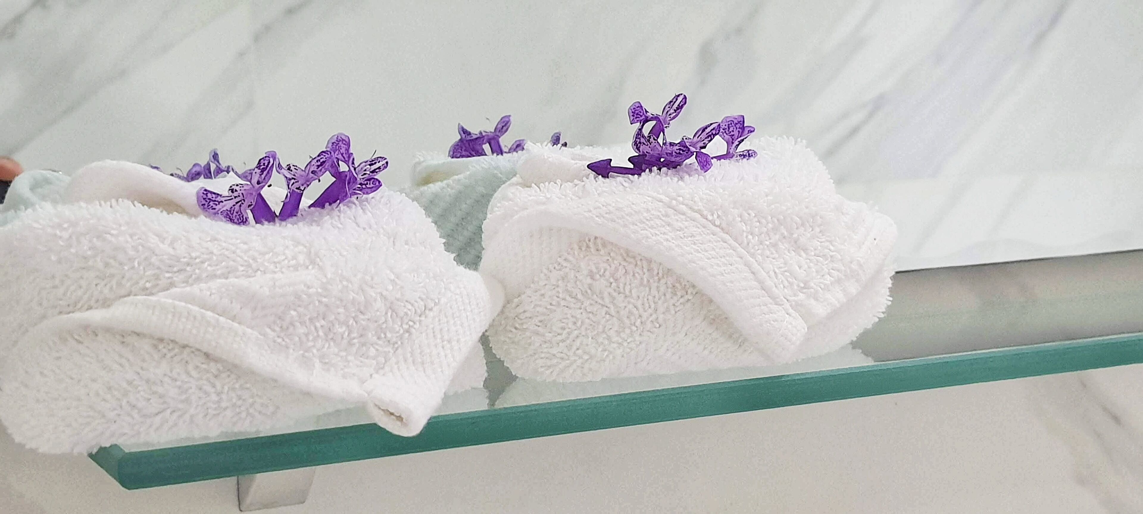 Two white towels with purple floral embroidery on a glass shelf.