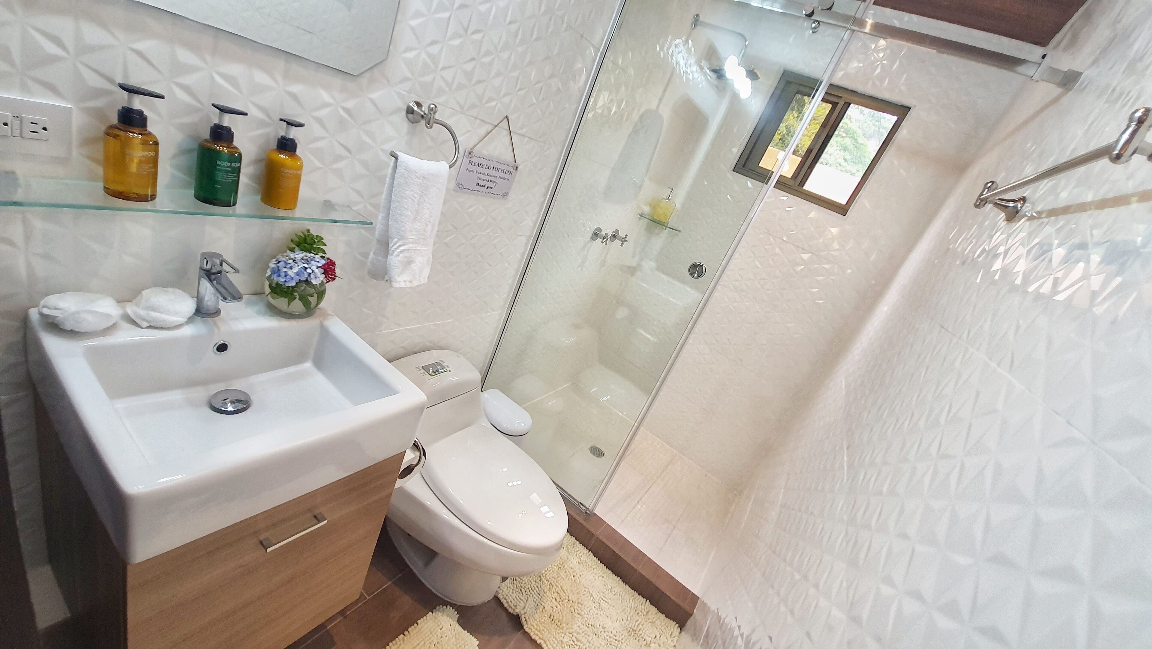 A modern bathroom with a glass-enclosed shower, a white sink with toiletries, and a toilet.