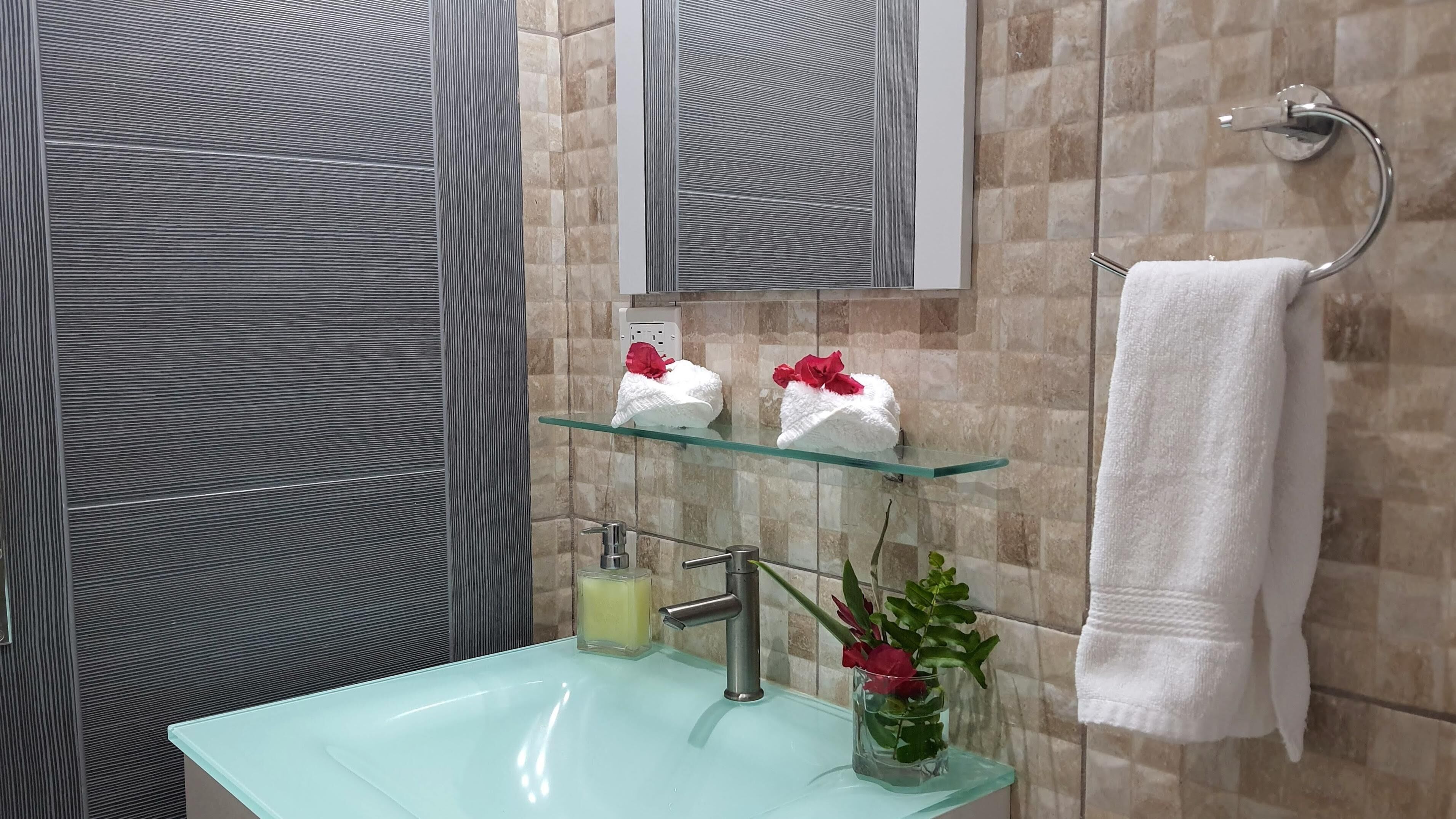 A bathroom with a glass sink, a mirror, a towel rack, and a glass shelf with towels and flowers.