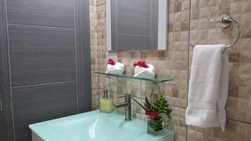 A bathroom with a glass sink, a mirror, a towel rack, and a glass shelf with towels and flowers.
