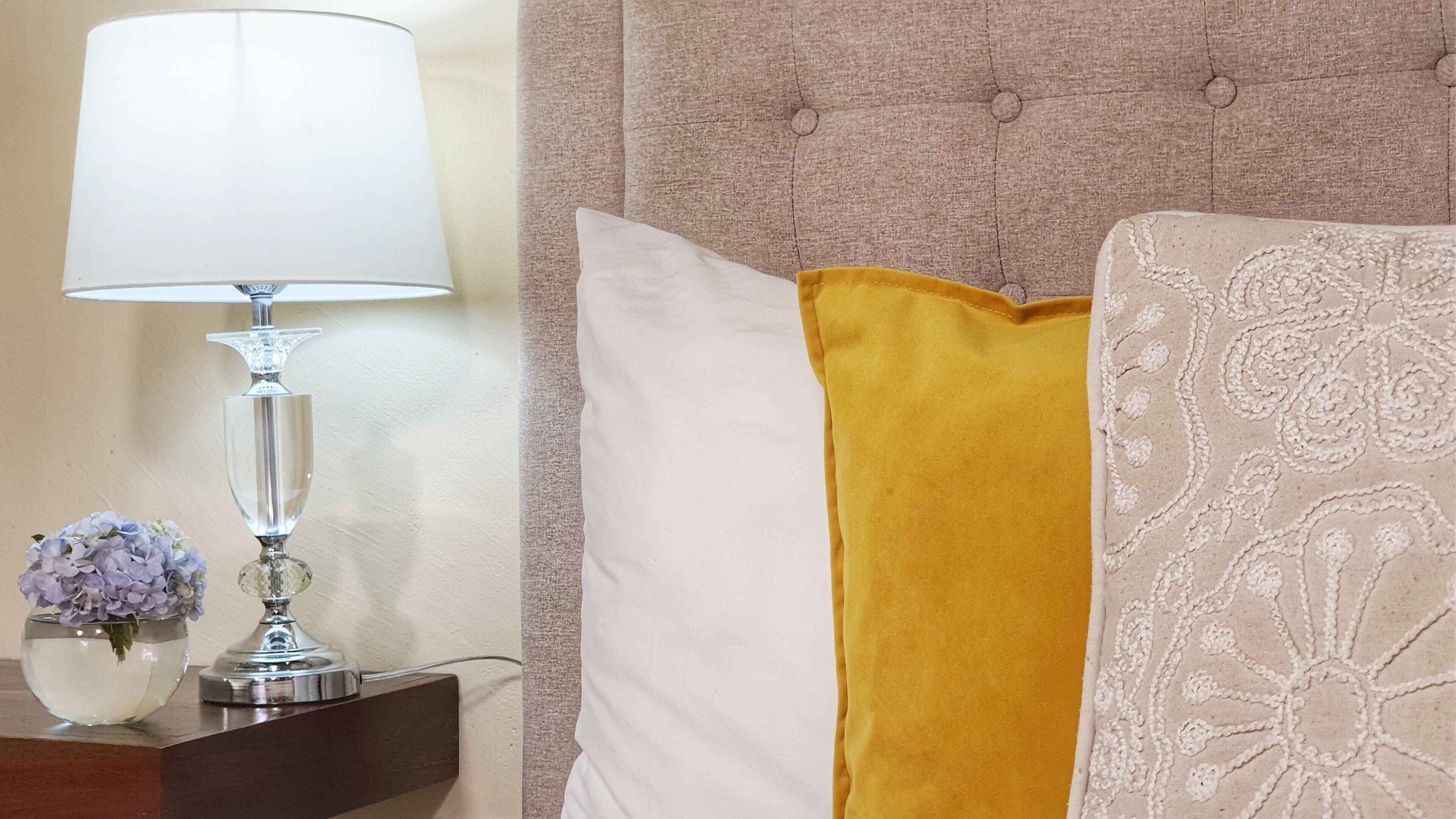 A neatly arranged hotel room with a bed, a bedside table with a lamp, and a vase of flowers.