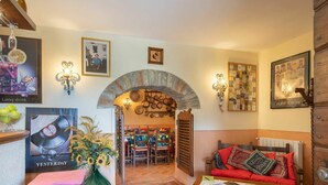Un accogliente soggiorno con un arco in pietra, un divano rosso, un tavolino in legno e un'area pranzo con sedie e tavolo.