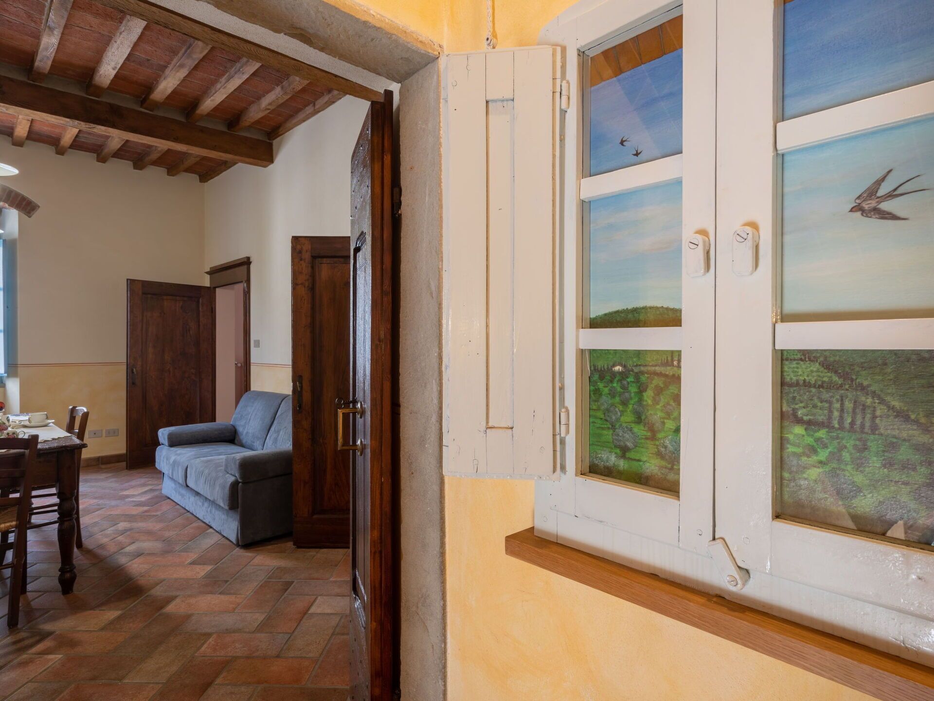 A room with a wooden ceiling, a dining table with chairs, a sofa, and a window with a view of a landscape.