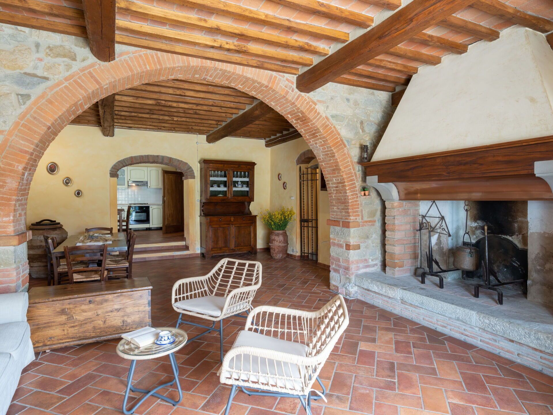Un intérieur rustique avec une cheminée en briques, des meubles en bois et une arche donnant sur la cuisine.