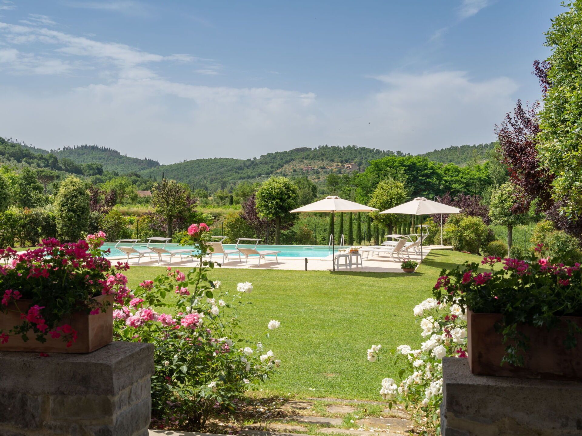 Un espace piscine agrémenté de chaises longues et de parasols, entouré d’une pelouse bien entretenue et de plantes en fleurs.
