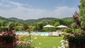 A pool area with lounge chairs and umbrellas, surrounded by a well-maintained lawn and flowering plants. - Beautiful private villa for 7 guests with private pool, WIFI, TV, patio and pets allowed (Castiglion Fiorentino)