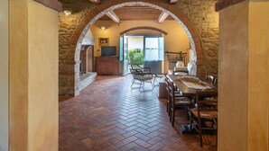 An arched stone corridor leading to a dining area with rustic wooden furniture and a television. - Beautiful private villa for 7 guests with private pool, WIFI, TV, patio and pets allowed (Castiglion Fiorentino)