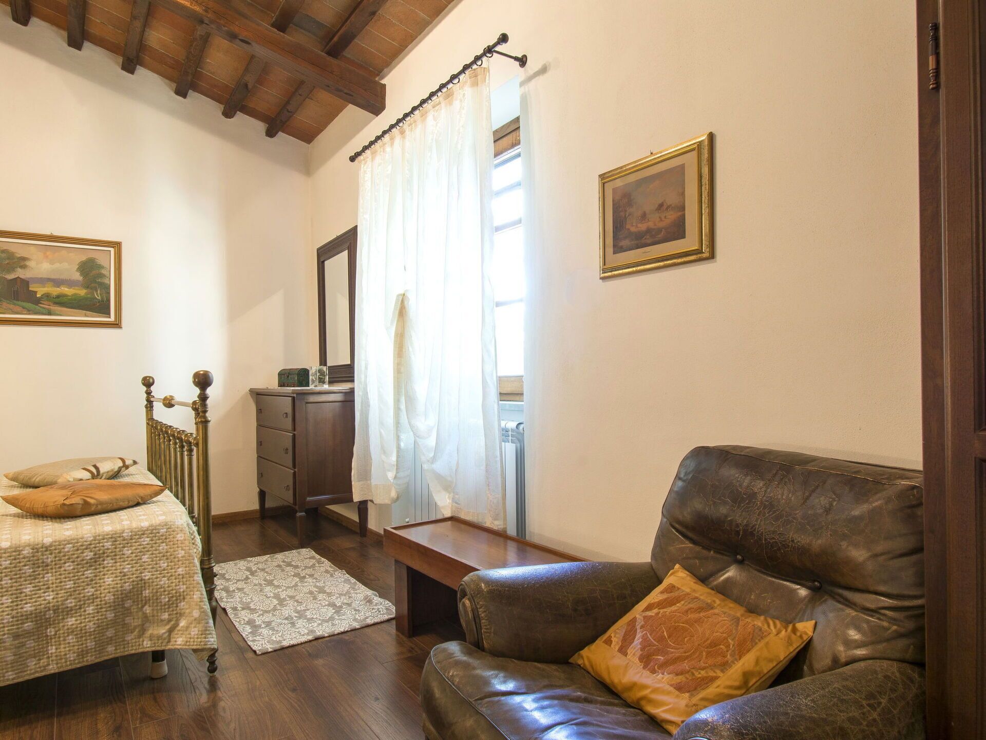 A cozy room with a bed, a leather armchair, a wooden dresser, and a painting on the wall.