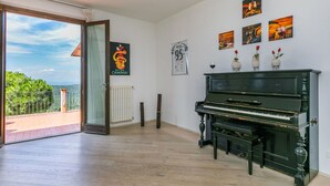 Ein geräumiger Raum mit einem Klavier, einer Heizung und einem großen Fenster mit Blick auf Grünflächen.