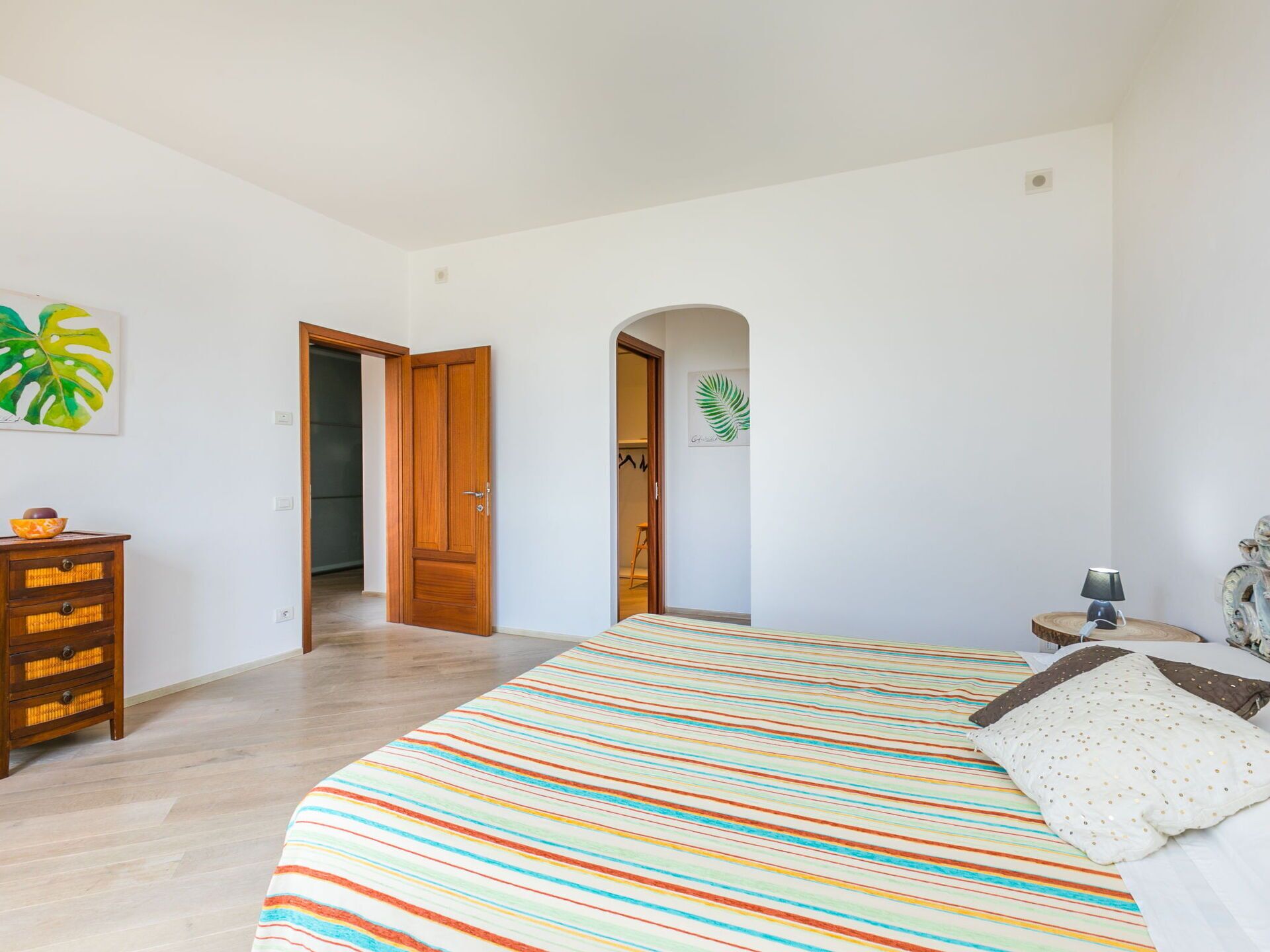 A bedroom with a large bed, wooden dresser, and a door leading to another room.