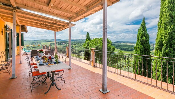 Eine überdachte Terrasse mit Esstisch, mit Blick auf eine reizvolle Landschaft mit Weinbergen und hohen Bäumen.