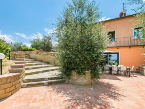 Una escalera de piedra que lleva a una casa con balcón, rodeada de olivos y un patio con mobiliario exterior.