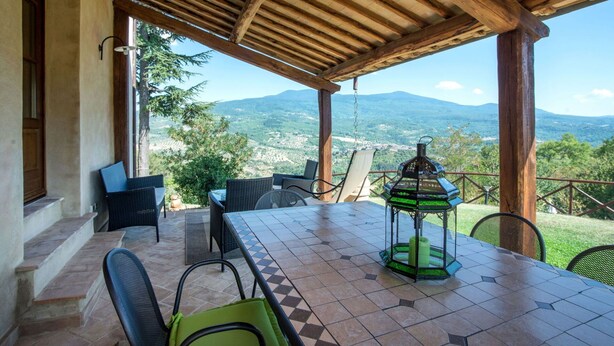 Ein überdachter Außenbereich mit Tisch und Stühlen, mit Blick auf eine gebirgige Landschaft.