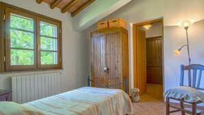 Een slaapkamer met een bed, een houten garderobe, een stoel, een lamp en uitzicht op het omliggende landschap door een raam.