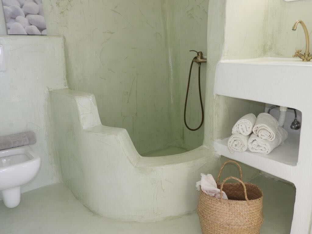 A bathroom with a white toilet, a shower with a handheld showerhead, and a sink with towels.