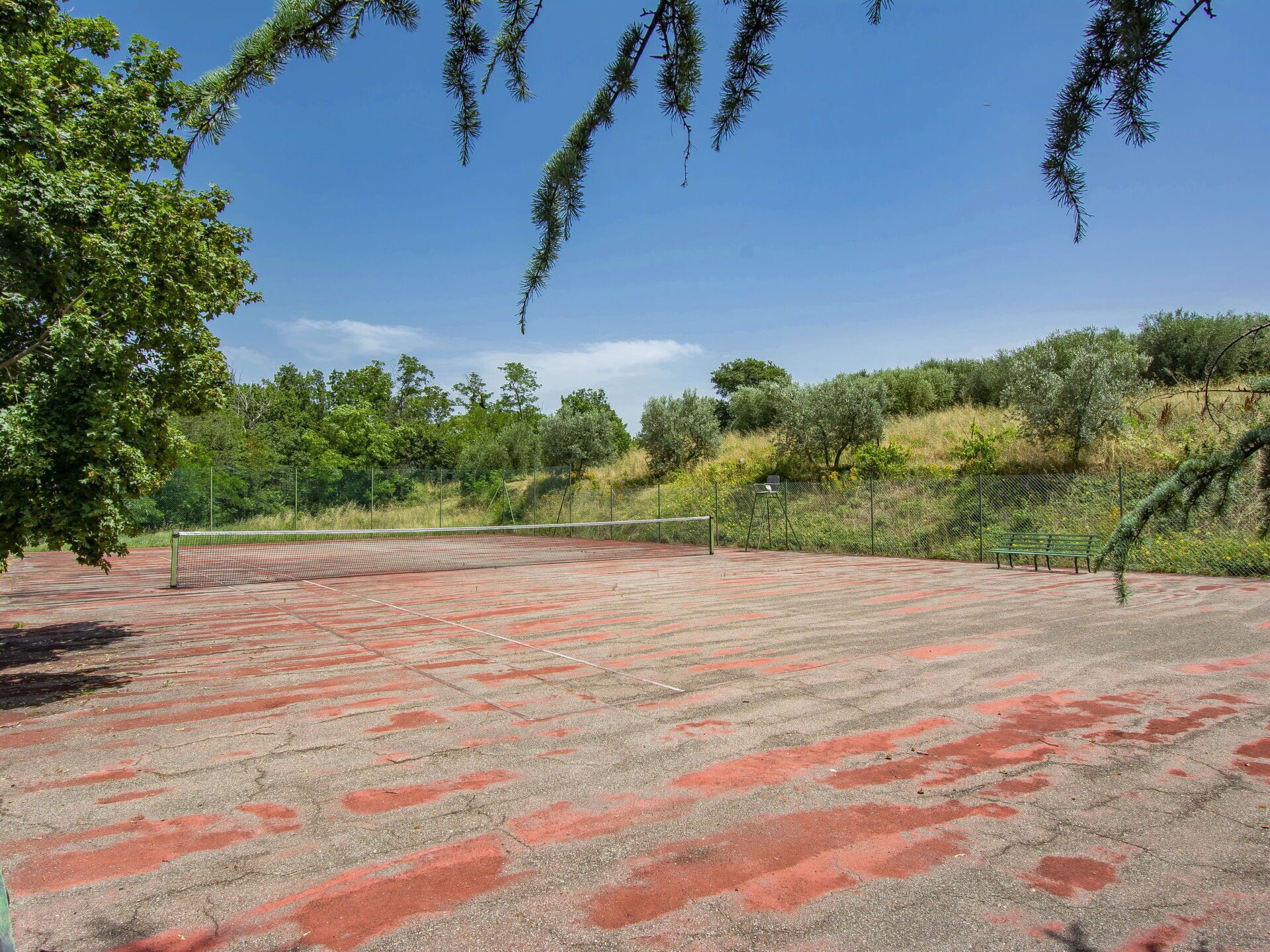 An outdoor tennis court with a net, surrounded by trees and a fence.