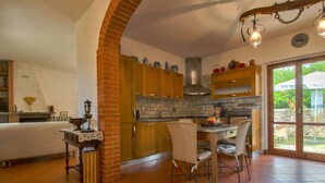 Une cuisine avec des meubles en bois, un pare-feu en carrelage et un coin repas avec des chaises en osier.
