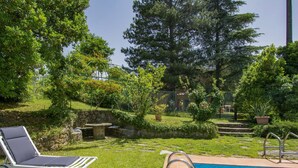 Une piscine avec un escalier en métal, une chaise longue et un mur en pierre.