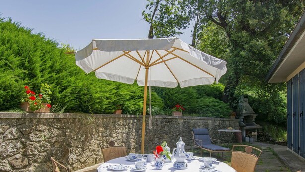Une table ronde dressée pour le thé, avec des nappes blanches, des chaises en osier et un parasol blanc.