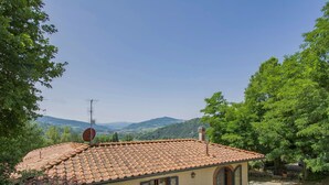 Une petite maison avec un toit en tuiles, une antenne parabolique et un jardin agrémenté d’un parasol.