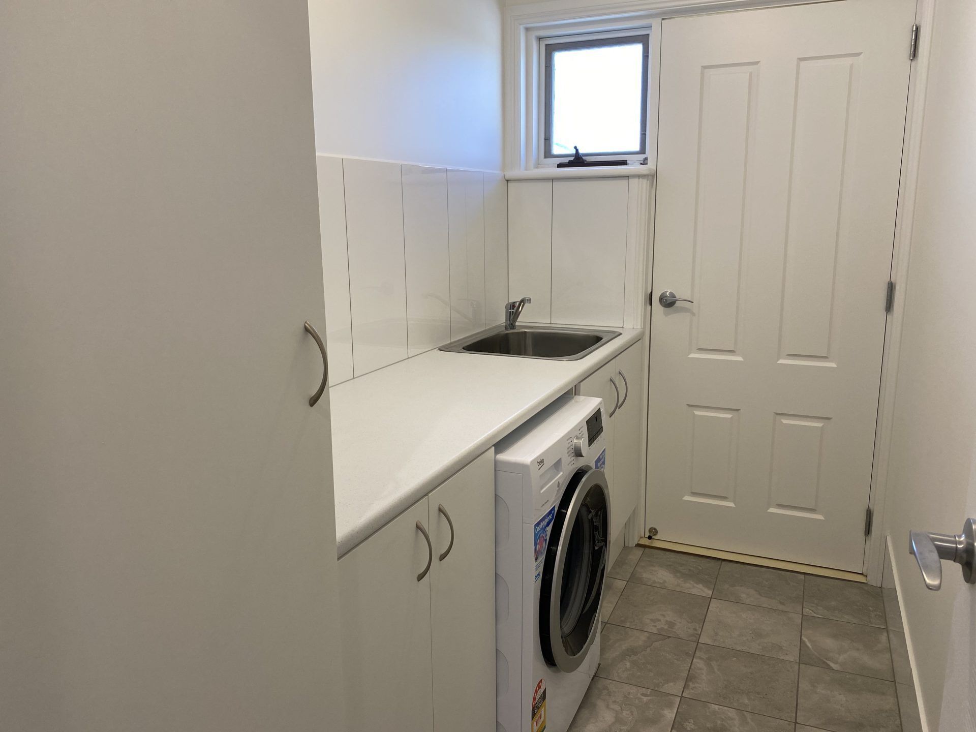 A compact laundry room with a washing machine, a sink, and a window above the sink.