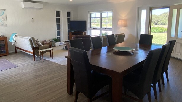 A spacious dining area with a large wooden table and modern chairs, a television, and a view of the outdoors through large windows. - The 19th Green - Located near the golf course! Pet Friendly - Outside Only (Robe)
