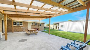 A covered patio area with a concrete floor, a wooden table, and blue plastic chairs. - The 19th Green - Located near the golf course! Pet Friendly - Outside Only (Robe)