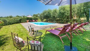A backyard with a swimming pool, lounge chairs, and a table with drinks.