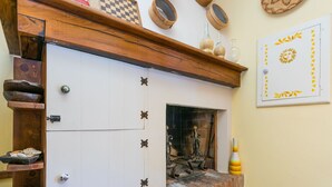 A rustic kitchen with a brick fireplace, wooden shelves, and a checkered wall decoration.