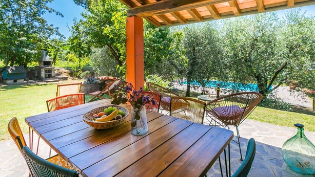An outdoor patio with a wooden table, wicker chairs, and a bowl of fruit.