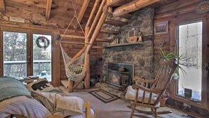 Un interior de cabaña acogedor con chimenea de piedra, vigas de madera, un sillón colgante y una mecedora.