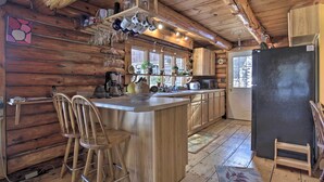 Cocina de cabaña de madera con una isla central, taburetes de bar, un refrigerador y un ventanal con vistas al exterior.