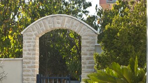 Un arc en pierre mène à une entrée fermée par un portail, l’ensemble étant entouré de plantes en pot et d’un mur de pierre.
