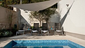 Un espace piscine extérieur doté d’une piscine carrelée, entouré de chaises longues et d’un auvent ombragé.
