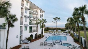 A hotel with a pool area, outdoor seating, and palm trees. - Oceanfront Condominium with pool (Saint Simons Island)
