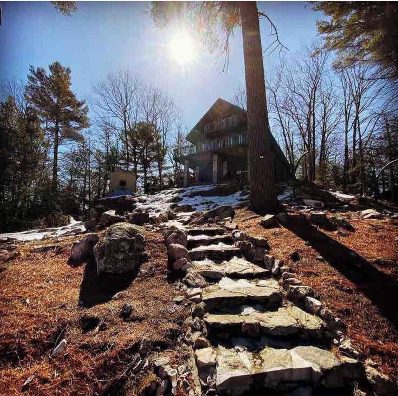 A stone pathway leading to a wooden cabin surrounded by trees and snow.