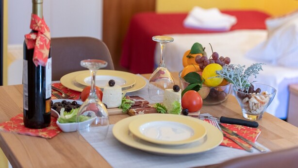 Een eettafel gedekt met borden, bestek, een fles wijn, een glas en een schaal fruit.