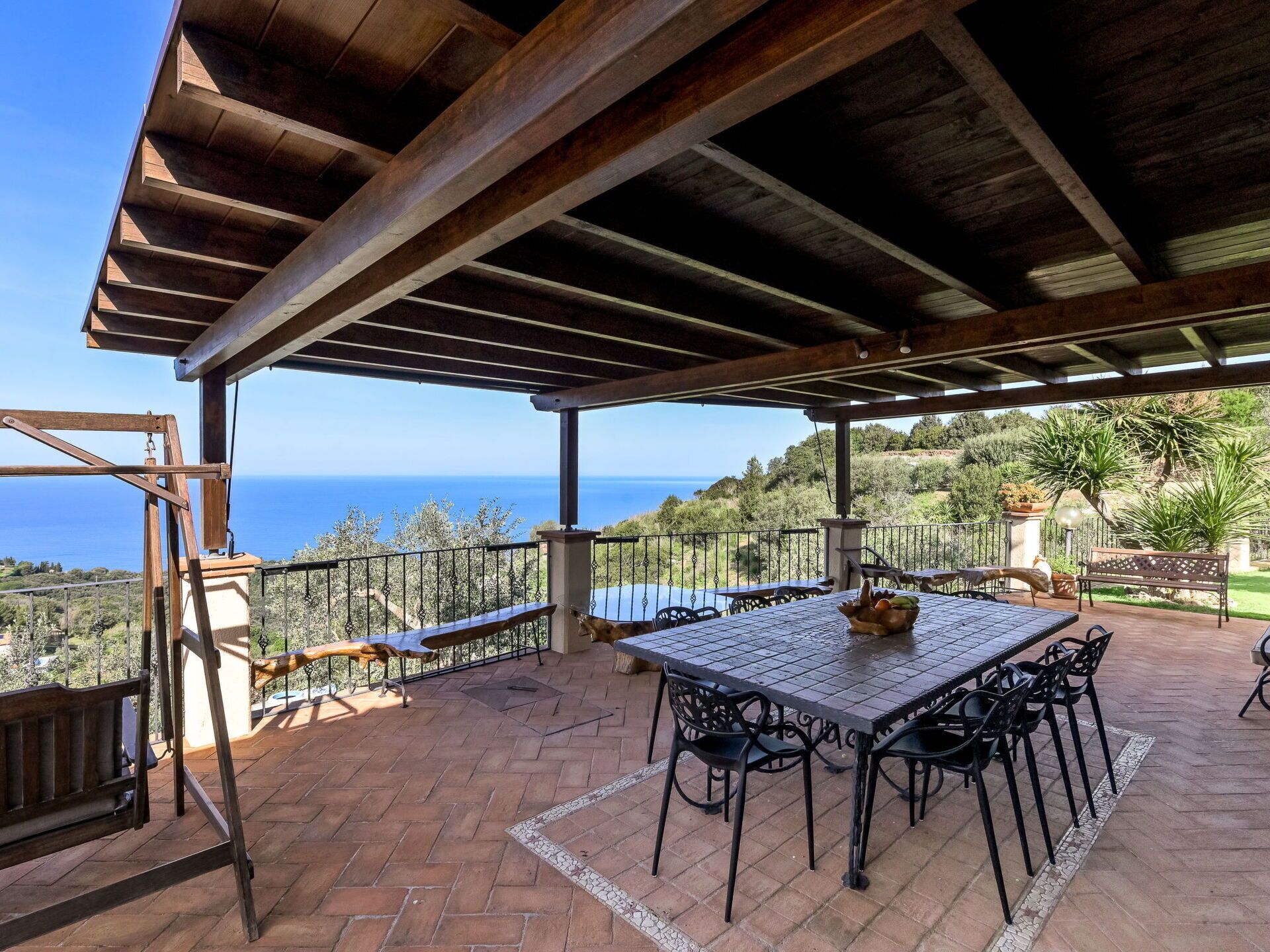 Une terrasse extérieure couverte, dotée d’une table et de chaises, offrant une vue panoramique sur la mer.