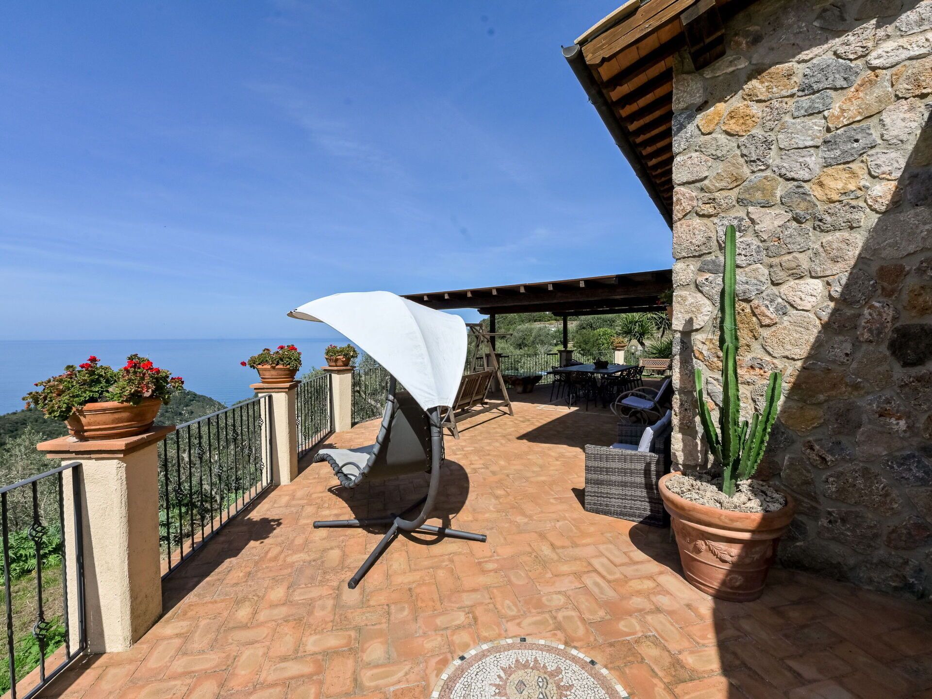 A terrace with a white umbrella, outdoor furniture, potted plants, and a stone wall.