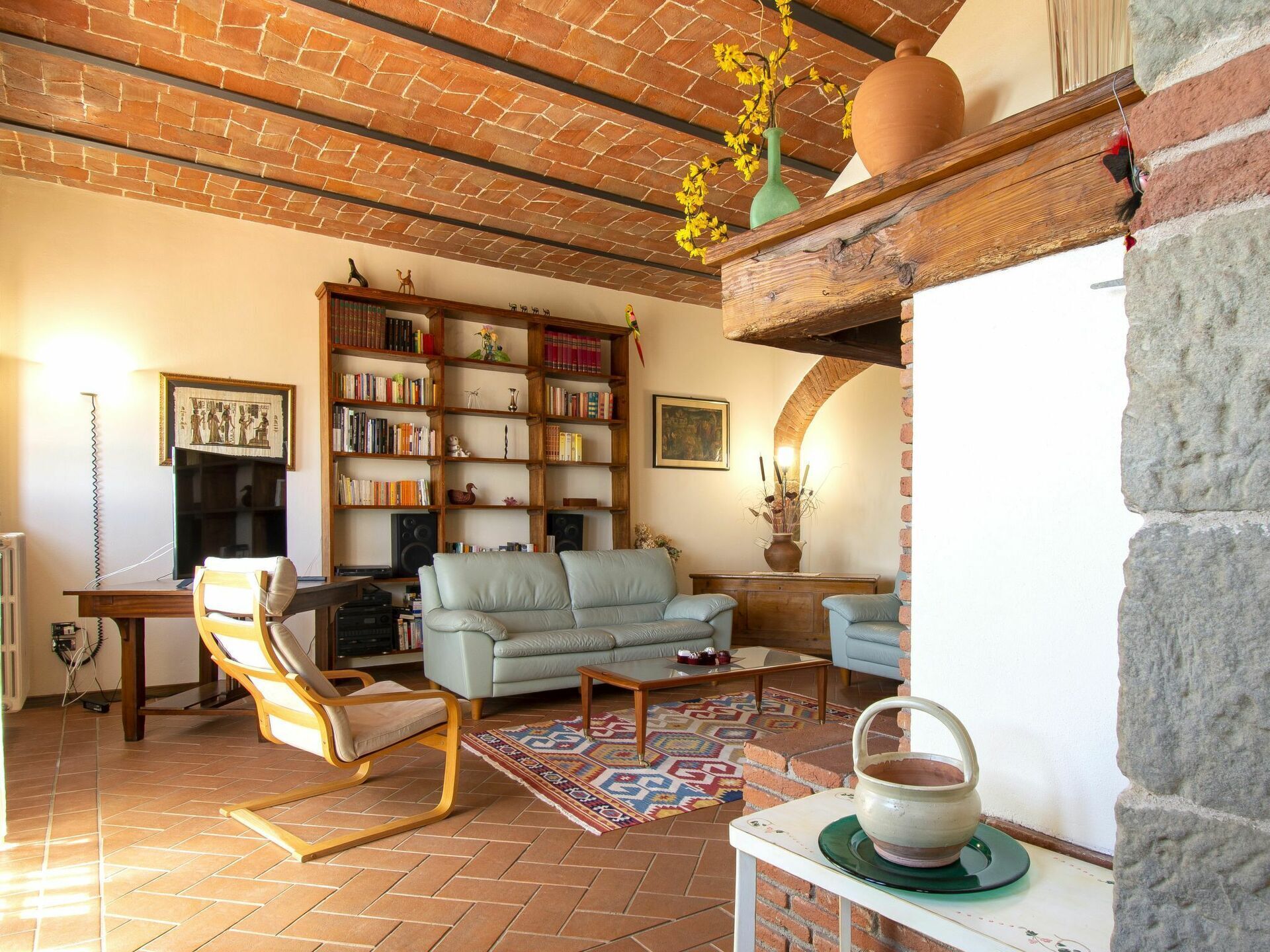 Ein gemütliches Wohnzimmer mit Kamin aus Backsteinen, einer Bücherwand voller Bücher, einem hellblauen Sofa und einem gemusterten Teppich.