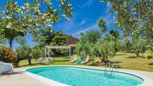 Una piscina con una pérgola, sillones de descanso y un patio de piedra.
