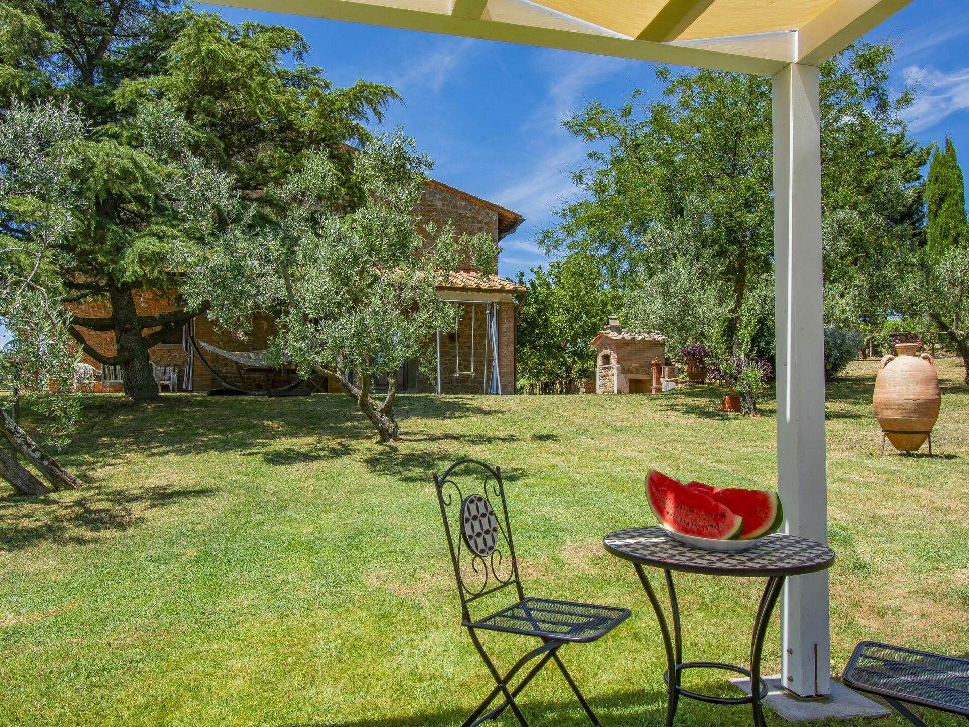 A patio area with a table and chairs, a large vase, and a pergola structure.