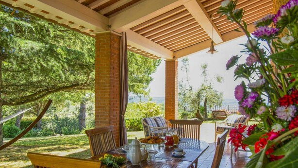 Un espacio de comedor al aire libre con techo, muebles de madera, un pilar de ladrillo y vistas al entorno verde y al paisaje.