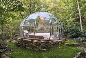 A transparent dome structure with a bed and seating area, surrounded by a stone wall and greenery. - Stunning private villa for 4 people with private pool, TV, patio and pets allowed (Camucia-monsigliolo)