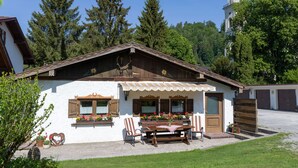Ein traditionelles Chalet mit Holzfassade, einem Essbereich mit Tisch und Stühlen und einem im Hintergrund sichtbaren Glockenturm.