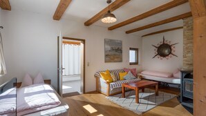 Ein gemütliches Zimmer mit Holzbalkendecke, einer Couch mit Kissen, einem kleinen Tisch und einem Kamin.
