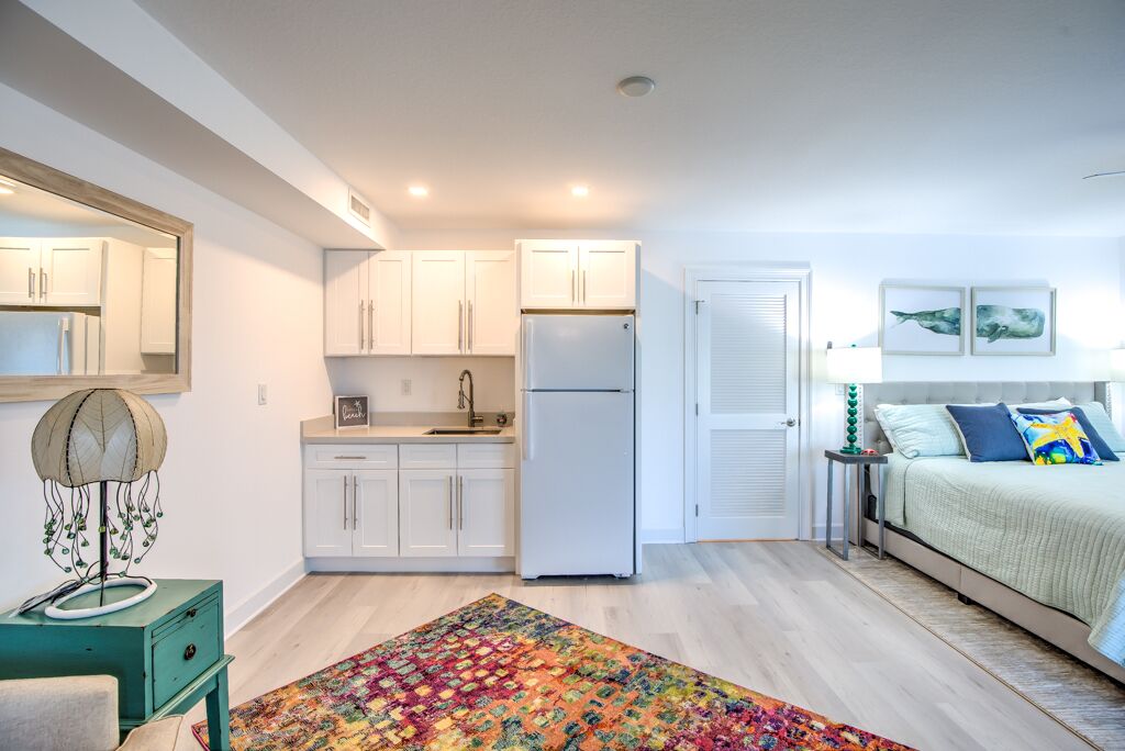 A compact living space with a kitchenette, a bed with colorful bedding, and a decorative lamp.