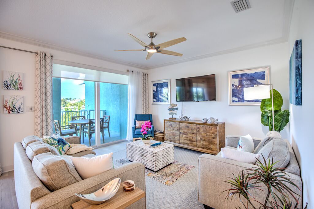 A living room with a sofa, coffee table, and TV. There is a balcony with a view.