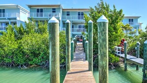A wooden pier leading to a building with balconies, surrounded by greenery and water. - Walk to Sombrero Beach! (Marathon)