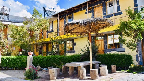 Un edificio amarillo con techo de paja, una mesa de piedra y una planta en maceta.